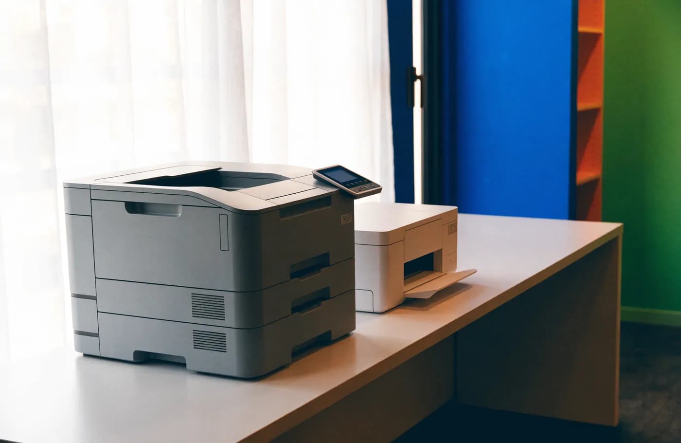 Une imprimante laser volumineuse et une imprimante jet d'encre compacte posées côte à côte sur un bureau